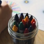 A child coloring with crayons in a jar, showcasing creativity and fun in art activities.