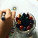 A child drawing with colorful crayons, fostering creativity and fun in a learning environment.
