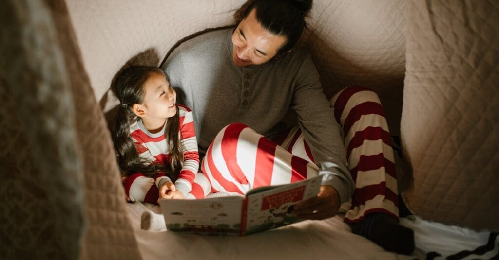Father and daughter enjoy a bedtime story under a cozy blanket, sharing smiles and bonding.