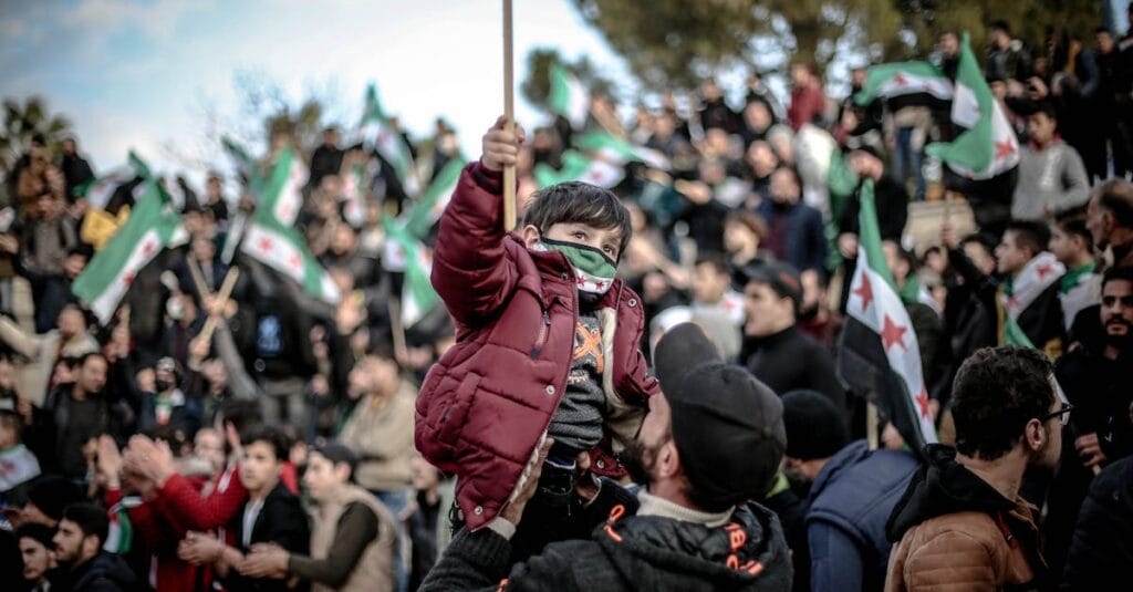Crowd gathers in Idlib, Syria for a protest, featuring a child with a flag.