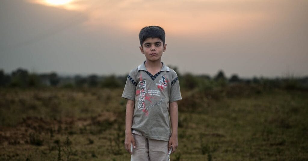 A contemplative boy stands alone in a grassy field at sunset, exuding calm.