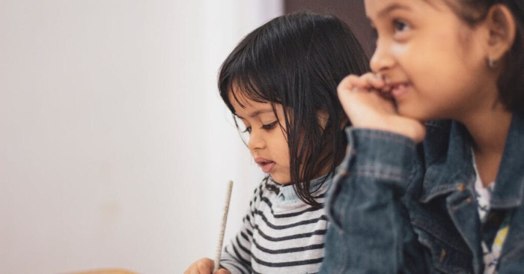 Two young girls joyfully engaged in creative learning indoors, capturing a candid moment of togetherness.