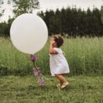 A happy child enjoying a large white balloon in a lush green field.