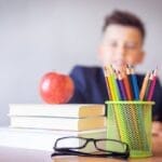 Schoolboy smiling behind a desk with books, pencils, and an alarm clock symbolizing study and creativity.