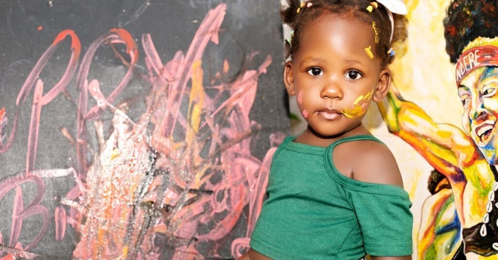 A charming child artist showcases her creativity in front of vibrant paintings.