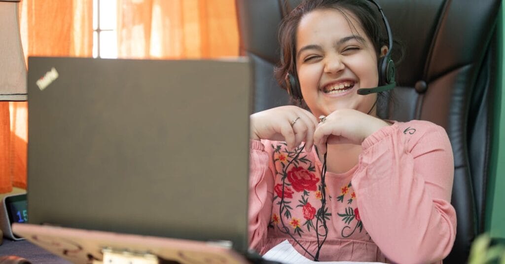 Smiling young girl with headset on a video call, studying online at home.