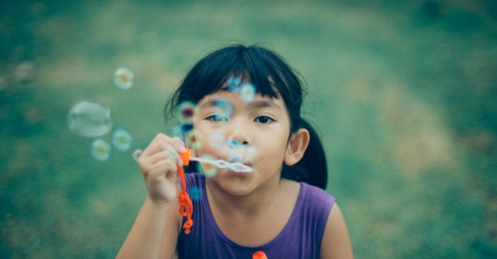 Adorable young girl enjoying summer outdoors while blowing bubbles, capturing pure childhood joy.