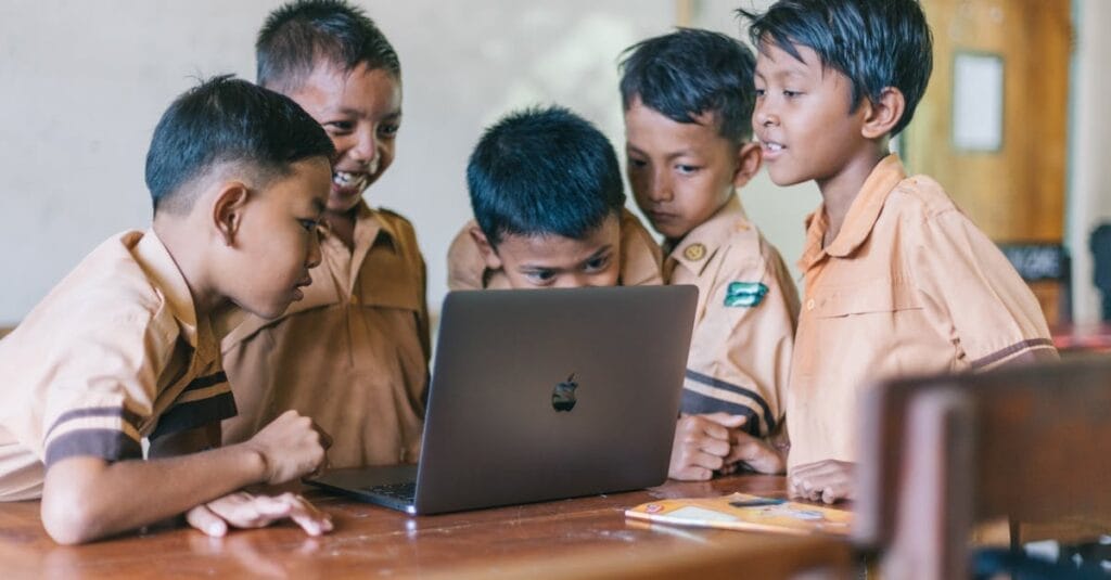 A group of young boys in school uniforms collaborating over a laptop in a classroom setting.