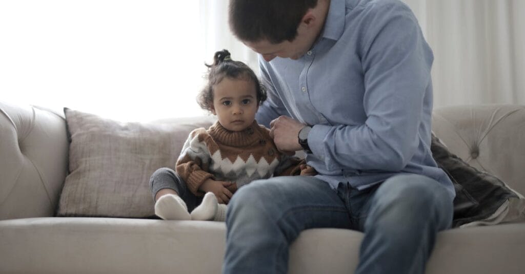 A father lovingly holds his child on a sofa, capturing a tender moment of parenthood indoors.