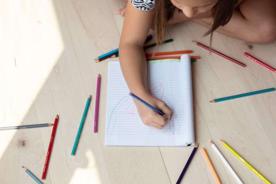 A young child drawing on paper surrounded by colorful pencils, illustrating creativity.