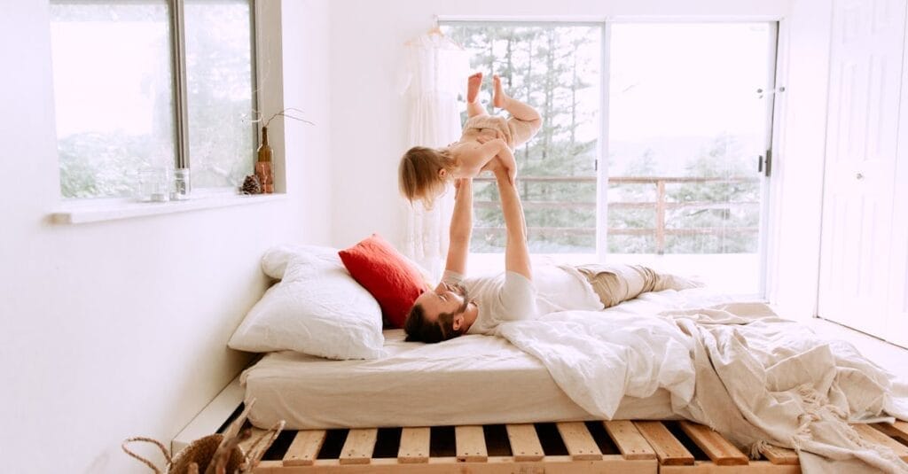 A father and daughter enjoying playful bonding time on a sunny morning in a cozy bedroom.