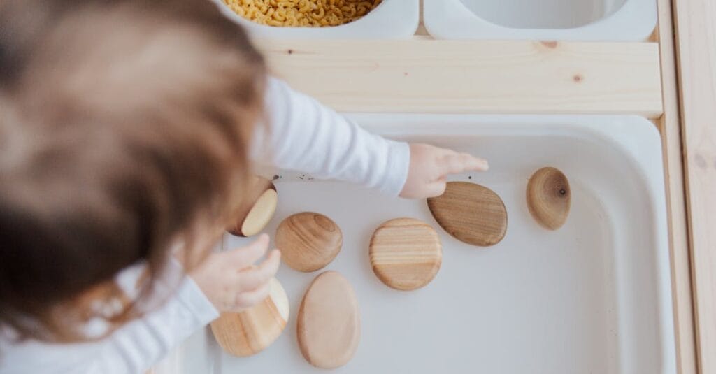 A toddler playing with wooden stones in a Montessori educational setup, promoting motor skills development.