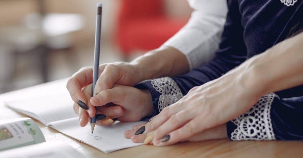 Close-up of hands guiding a child as they write in a notebook. Educational support scene.