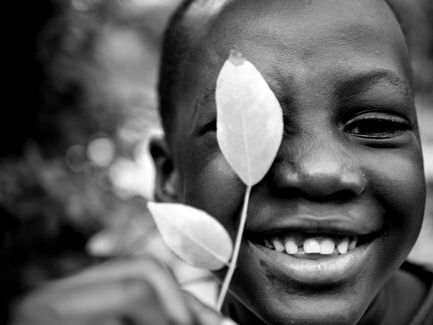 Close-up of a smiling child holding a leaf, captured in monochrome for an artistic touch.