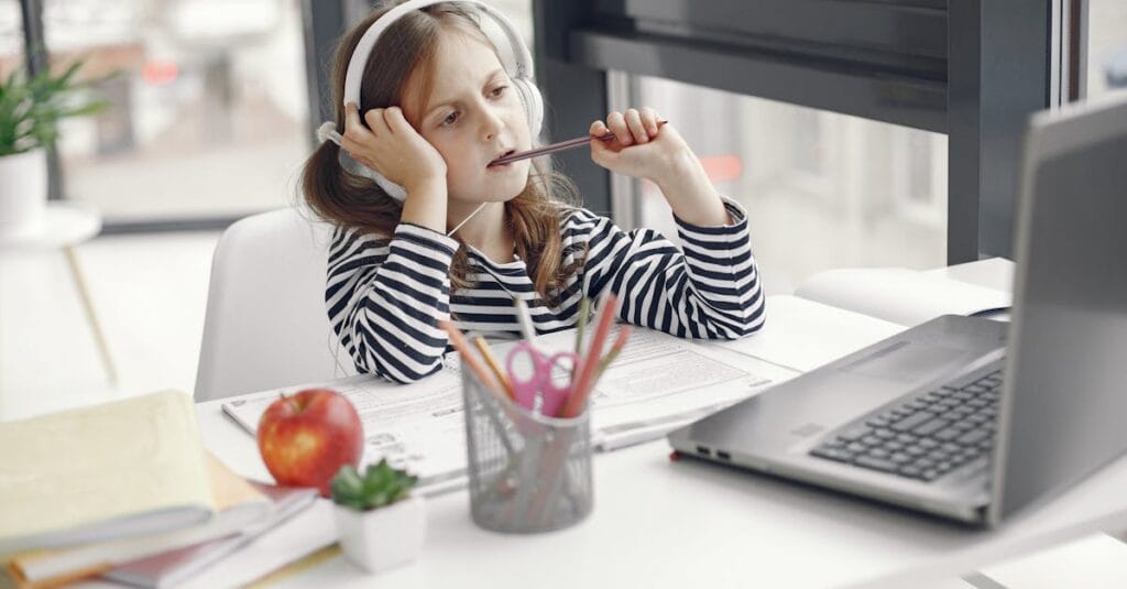 A child wearing headphones doing homework on a laptop indoors. Remote learning setup.