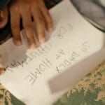 A child's hands writing a Christmas list on paper, emphasizing the joy of holiday preparations.