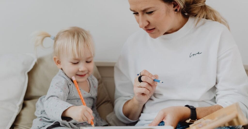 A mother and her toddler daughter draw together, sharing a heartwarming moment indoors.