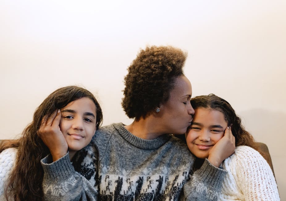 A joyful mother kissing her smiling daughters indoors, capturing love and family warmth.