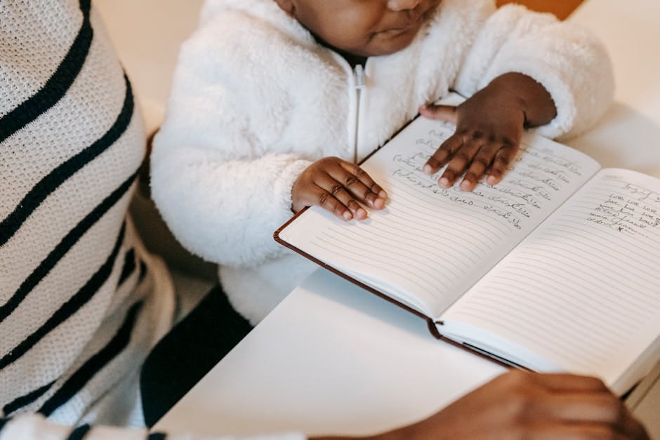 High angle of crop unrecognizable ethnic curious baby examining notepad near lady in casual outfit at table in bright apartment