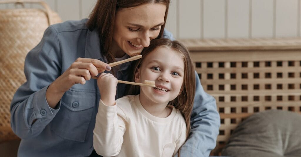 A joyful moment of a mother helping her daughter brush teeth indoors.