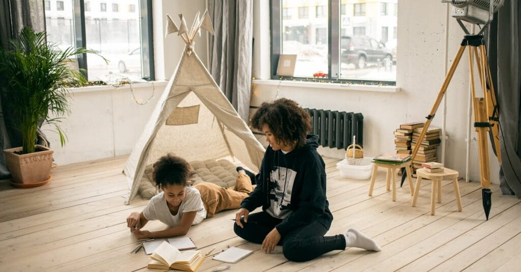 High angle of African American mother sitting on floor near girl reading book near play tent in studio