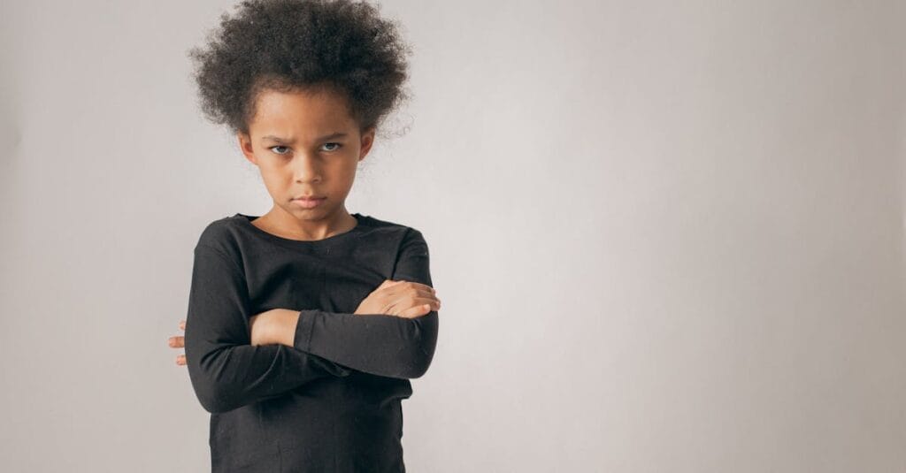 Portrait of a young child with crossed arms and a serious expression in a studio setting.