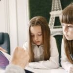 Two girls attentively studying with a tutor in a classroom setting.