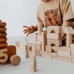 A child is building structures with wooden blocks in a playroom, focusing on creativity and learning.
