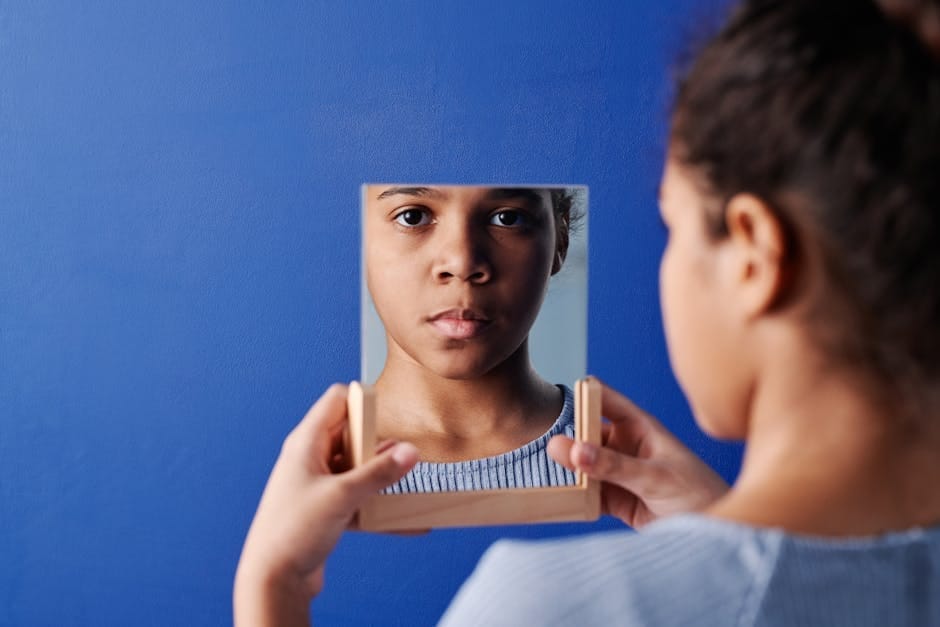 A young girl holds a mirror, reflecting her face, set against a vivid blue background.
