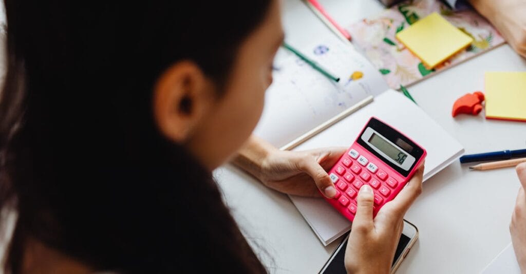 Young girl solving math problems with a pink calculator indoors.