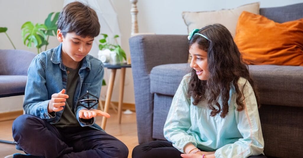 Smiling siblings playing with a spinning top on the floor in a cozy living room.