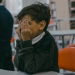 A child with hands covering face, experiencing bullying in a school setting.