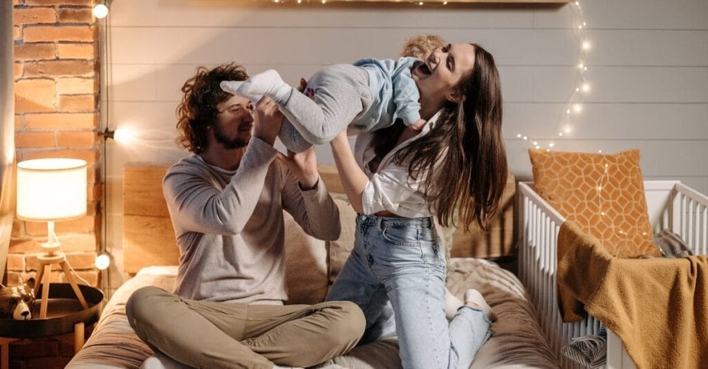 Joyful parents playing with their child on a bed in a warmly lit bedroom.