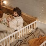 A father and child enjoy a bedtime story together in a warmly lit bedroom.