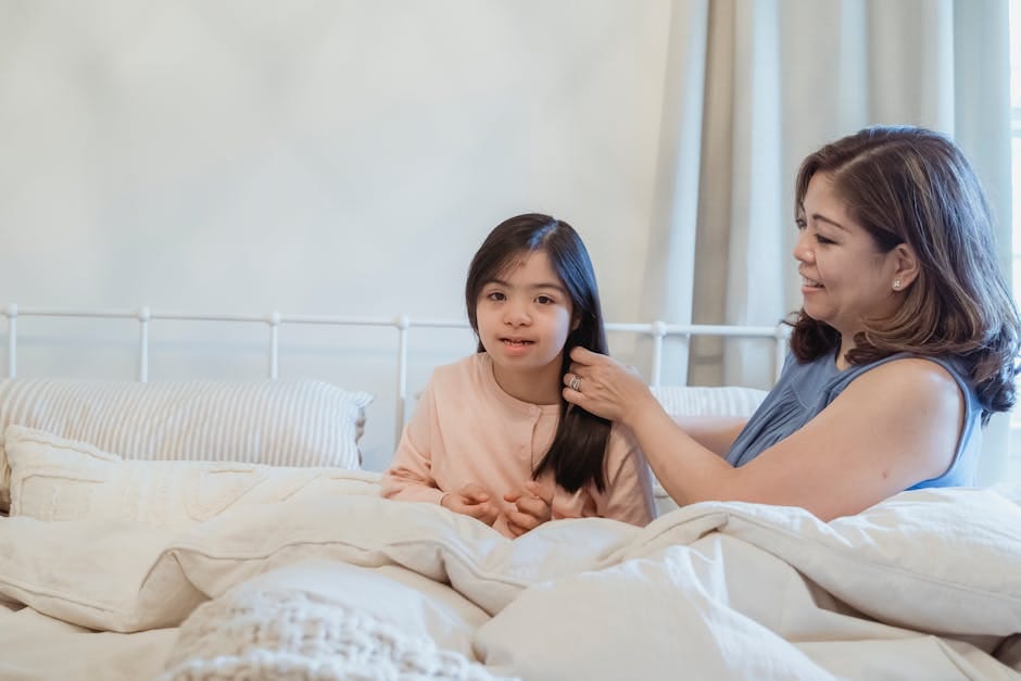 A mother lovingly fixes her daughter's hair on a cozy bed, capturing a moment of bonding and care.