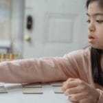 Young Asian girl with Down Syndrome engaged in a game indoors, wearing a pink sweater.
