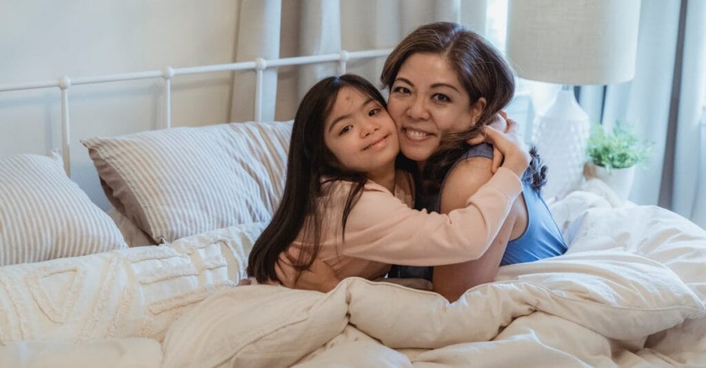 A mother and daughter happily embrace on a comfy bed, showcasing love and connection indoors.