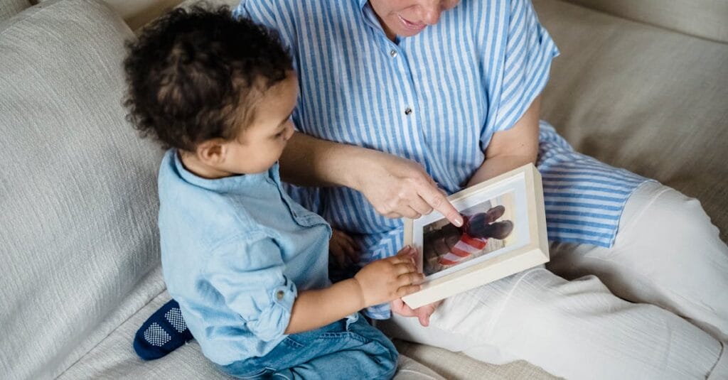 Grandmother and toddler bonding while looking at family photos on the sofa.