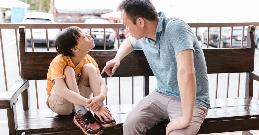 A heartfelt interaction between father and son sitting on a wooden bench outdoors, promoting bonds and autism awareness.