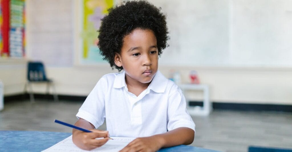 A focused young boy with afro hair writing in a classroom setting, showcasing education and learning.
