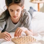 A young girl playing with a wooden geoboard on a bed, fostering creativity and learning.