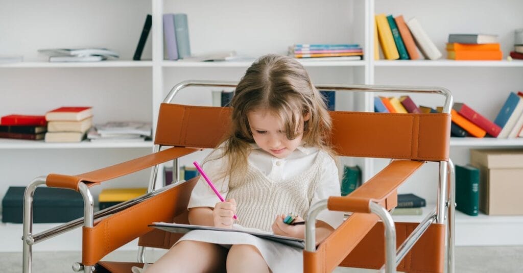 Caucasian girl sitting in a chair drawing with colored pencils in a cozy home library.
