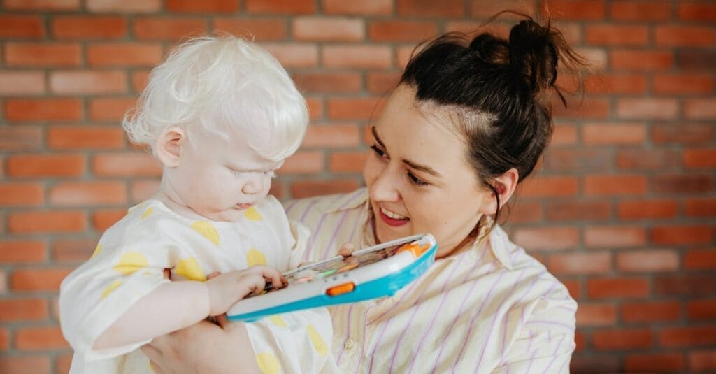 A loving mother holds her albino child while reading from a digital device at home.