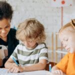 Teacher guides children in a creative classroom activity, focusing on learning and interaction.