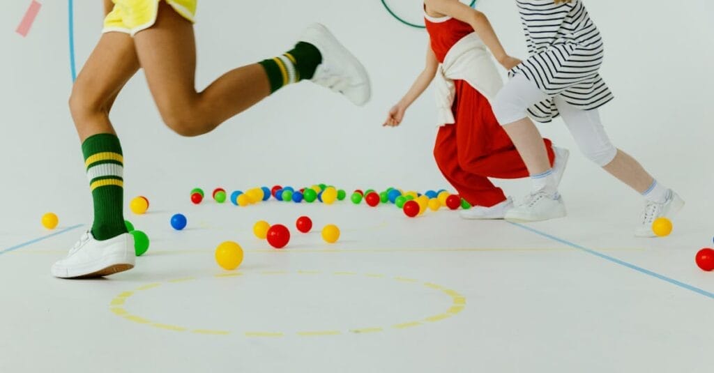 Children energetically playing with colorful balls in a bright indoor gym setting.