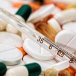 Close-up image showing various pills and a thermometer, emphasizing health and medicine.