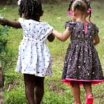 Two young girls in colorful dresses walking hand in hand outdoors, embodying friendship and innocence.