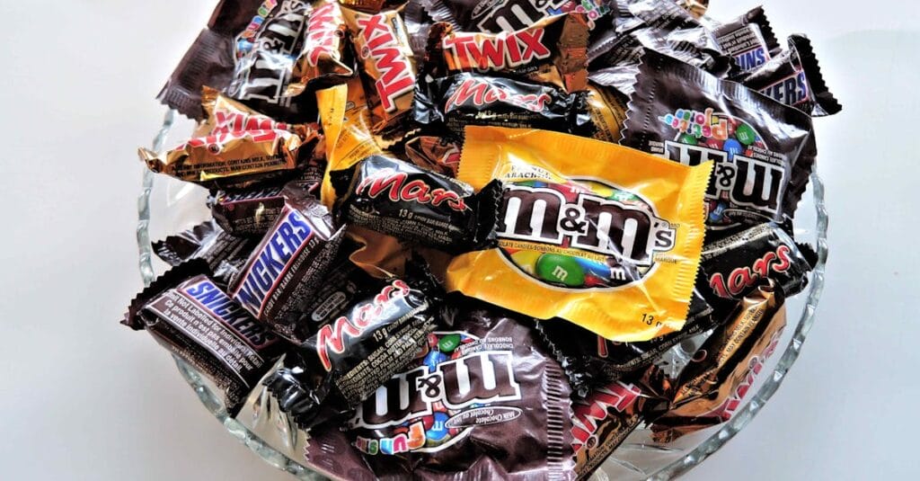 A bowl filled with various chocolate candies, including Twix, Snickers, and M&Ms, creating a vibrant dessert spread.