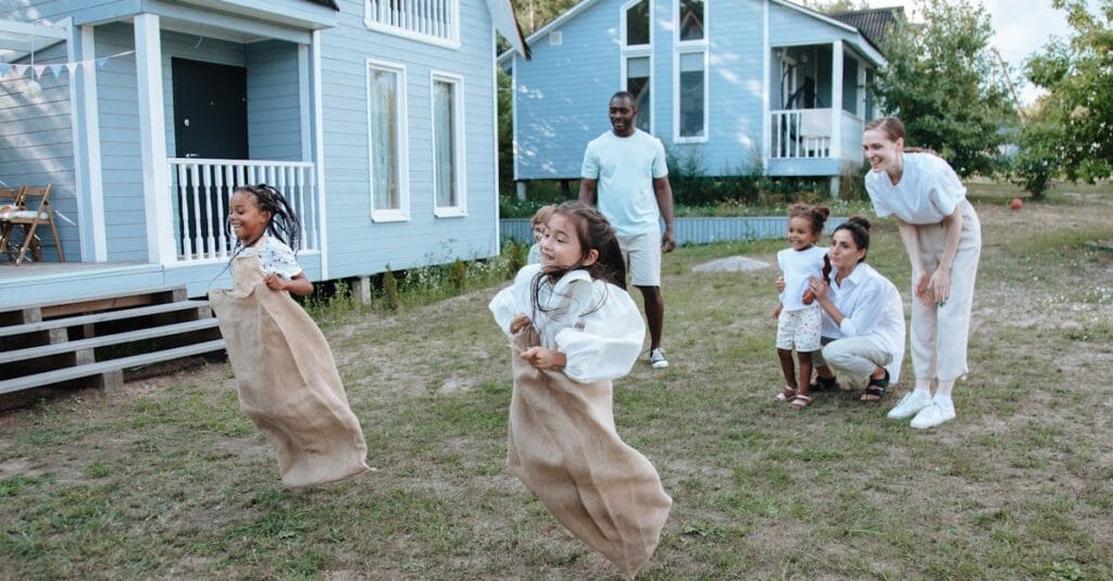Group of children enjoying a sack race in a backyard setting, surrounded by family.