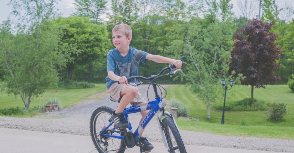 A young boy enjoys cycling outdoors in a lush green setting on a sunny day.